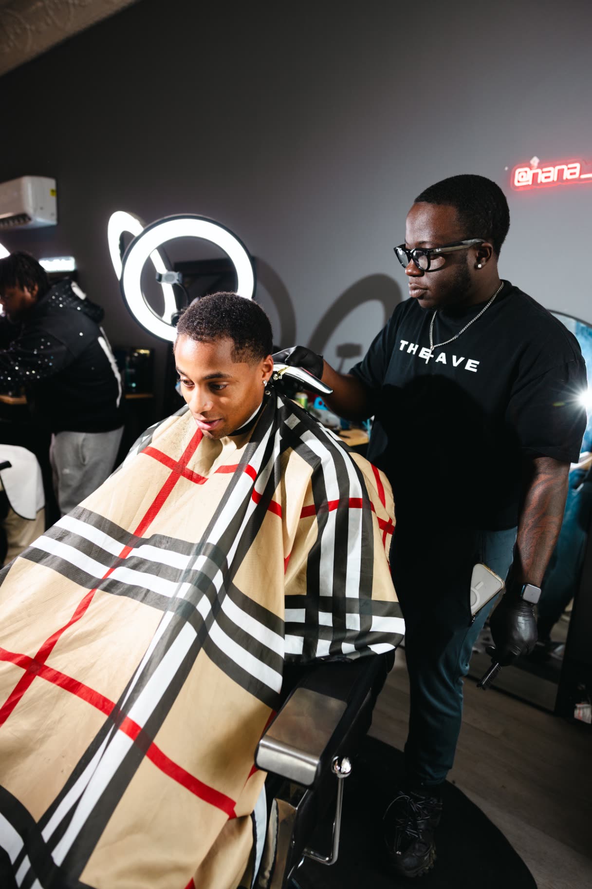 A barber shaping a lineup under ring light at The Ave